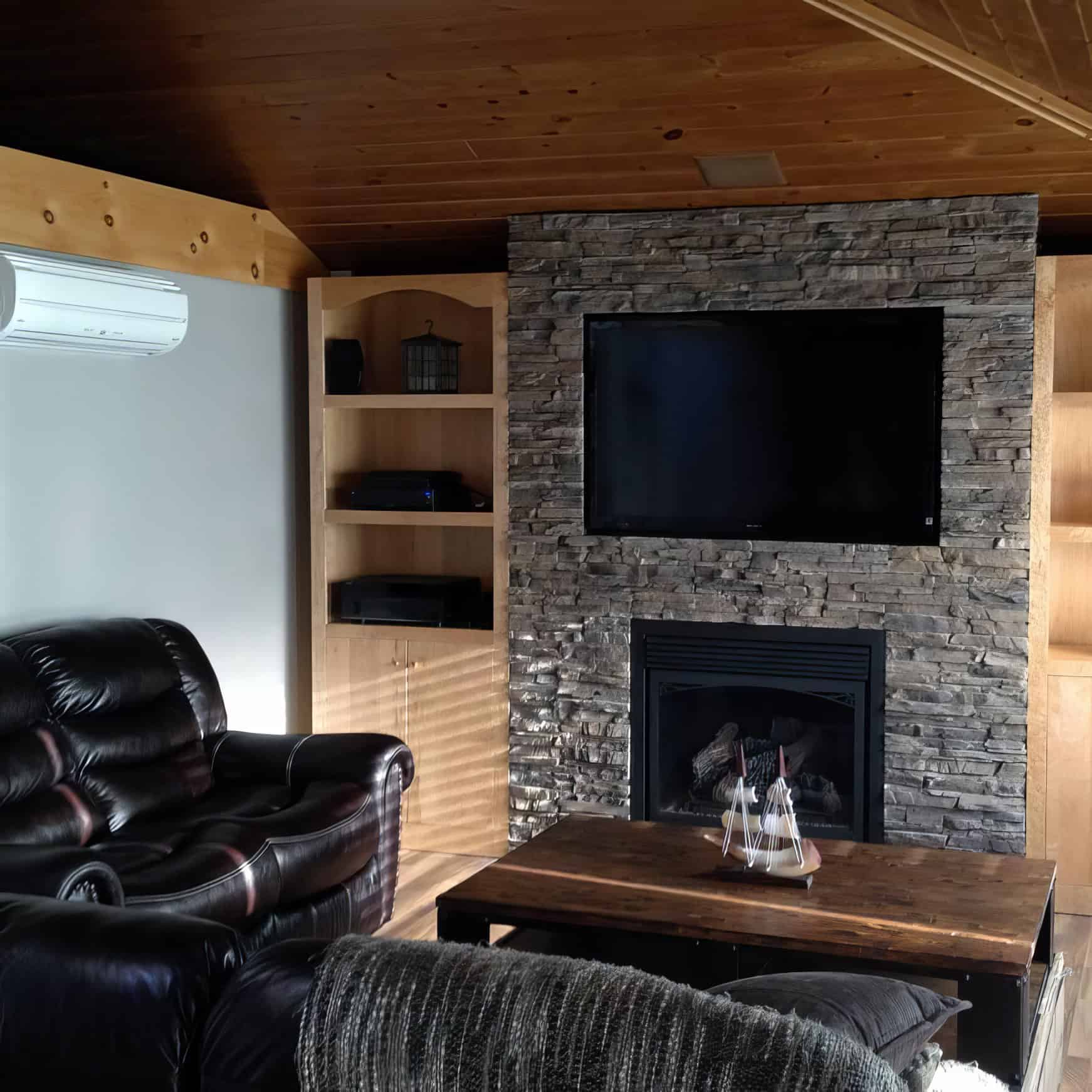 Conjunto de sala de estar con chimenea y televisión en pared de piedra.